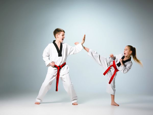 Two children practicing martial arts with red belts in a studio.