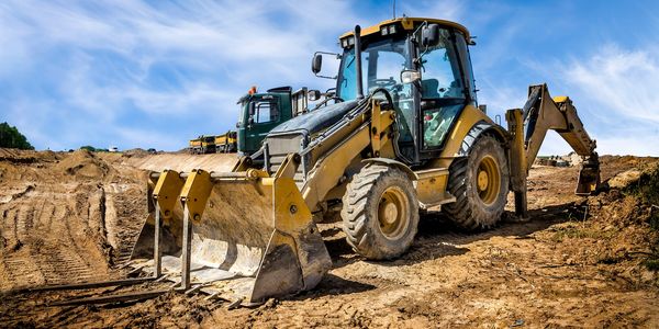 A yellow backhoe loader on a construction site with a clear sky.