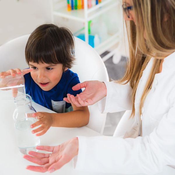 Young boy pouring water with adult supervision in a bright room.
