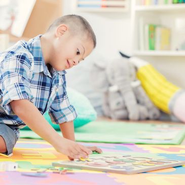 A young boy with Down syndrome playing with an alphabet puzzle on a colorful mat.