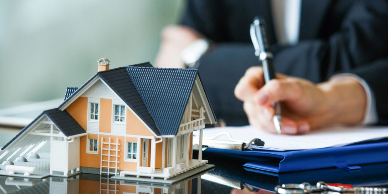 A person signing documents with a house model on the table.