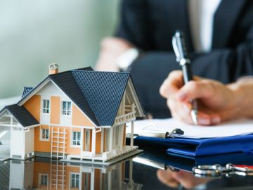A person signing documents with a house model on the table.