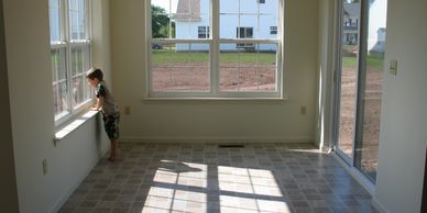 A young boy looks out a window in an empty sunlit room.