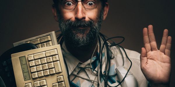 Man with glasses holding old keyboard and waving, tangled in cables.
