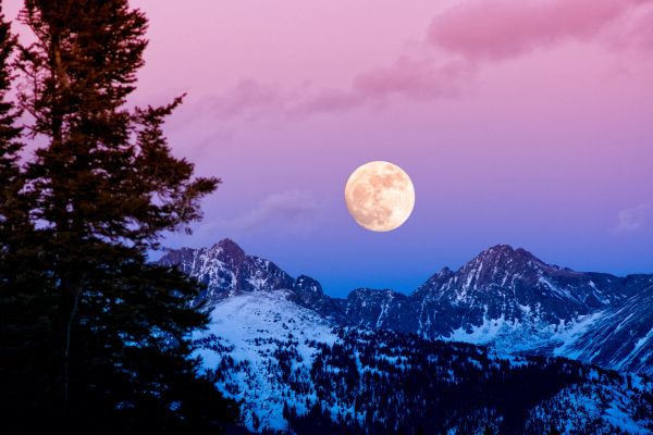Full moon rising over snowy mountains at dusk.