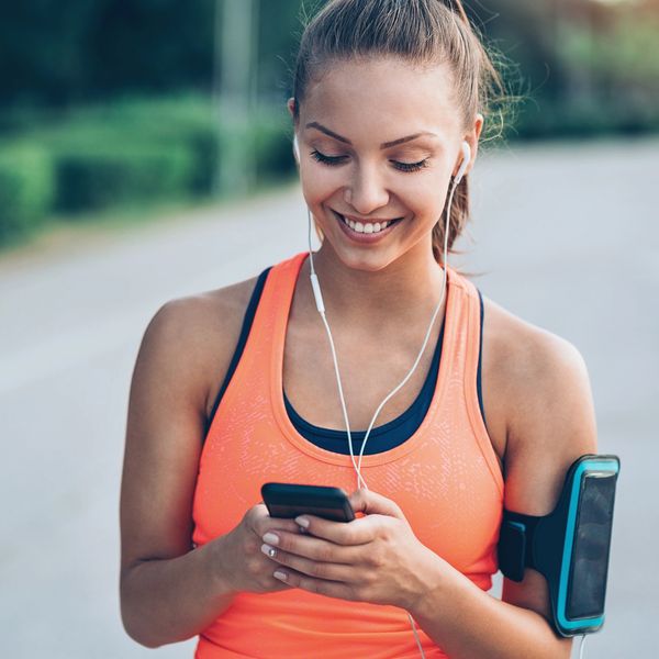 Smiling woman in sportswear using smartphone and earphones outdoors.