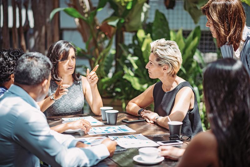 Group of professionals having a business meeting in outdoor cafe or restaurant where they discuss the investment ideas and cooperation plans while drinking coffee. Group of businesswomen and businessmen enjoying working together