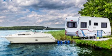 A white boat docked near a caravan by a lake under a cloudy sky.