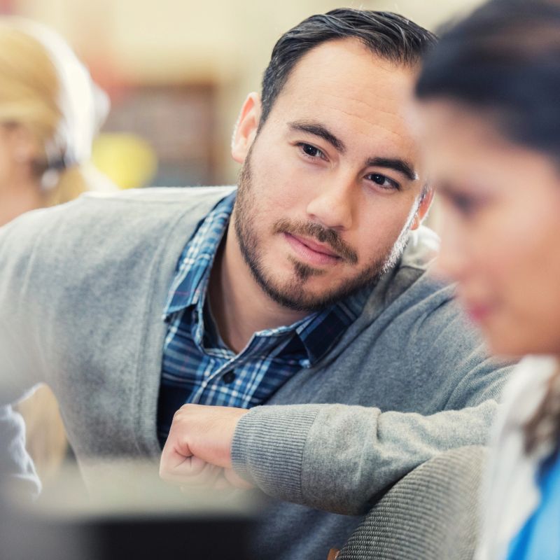 Handsome Hispanic college student helps female classmate with assignment.