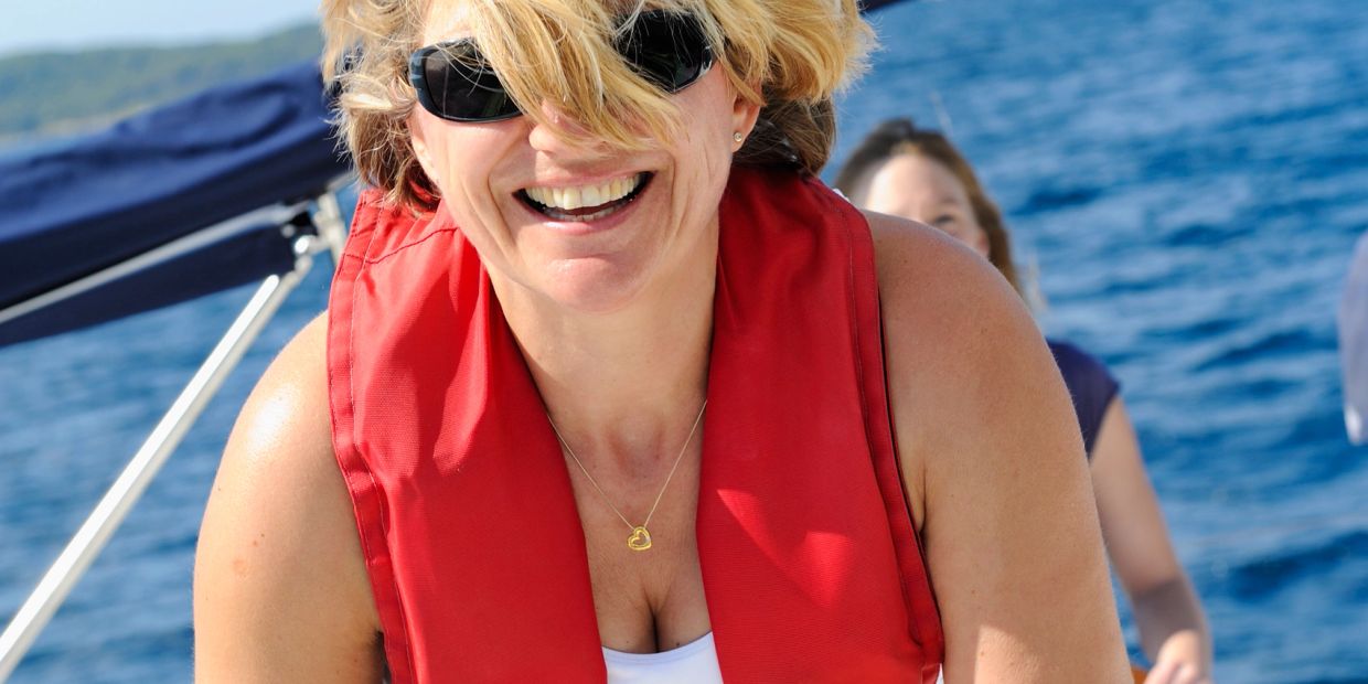 Woman smiling on a boat wearing a red life jacket and sunglasses.