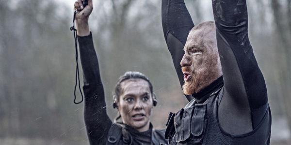Two intense, muddy athletes raising their arms in victory during an outdoor challenge.