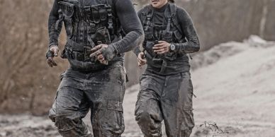 Two soldiers running in muddy terrain.
