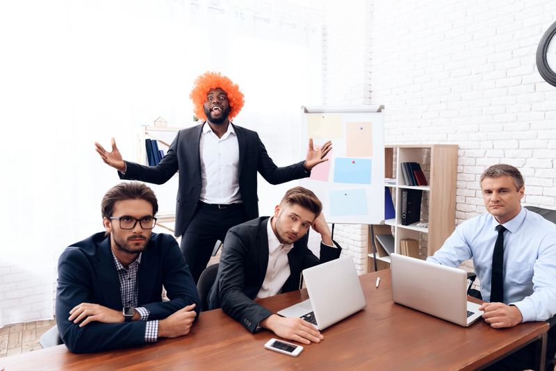 A man in a wig came to a business meeting. His colleagues are surprised. He jokes over them. He celebrates the April Fools Day.