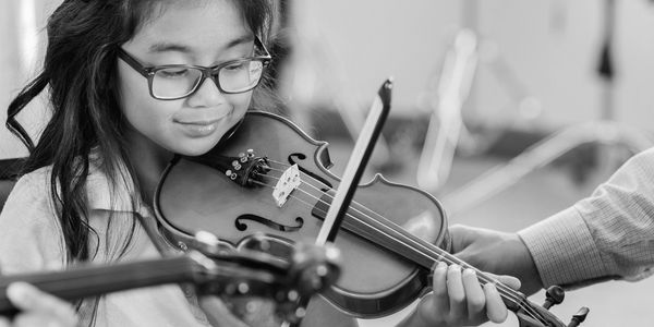 A young girl playing the violin with guidance.