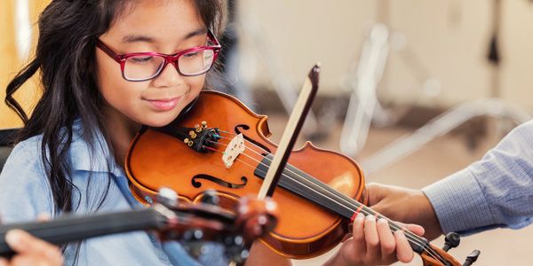 A young girl playing the violin with guidance.