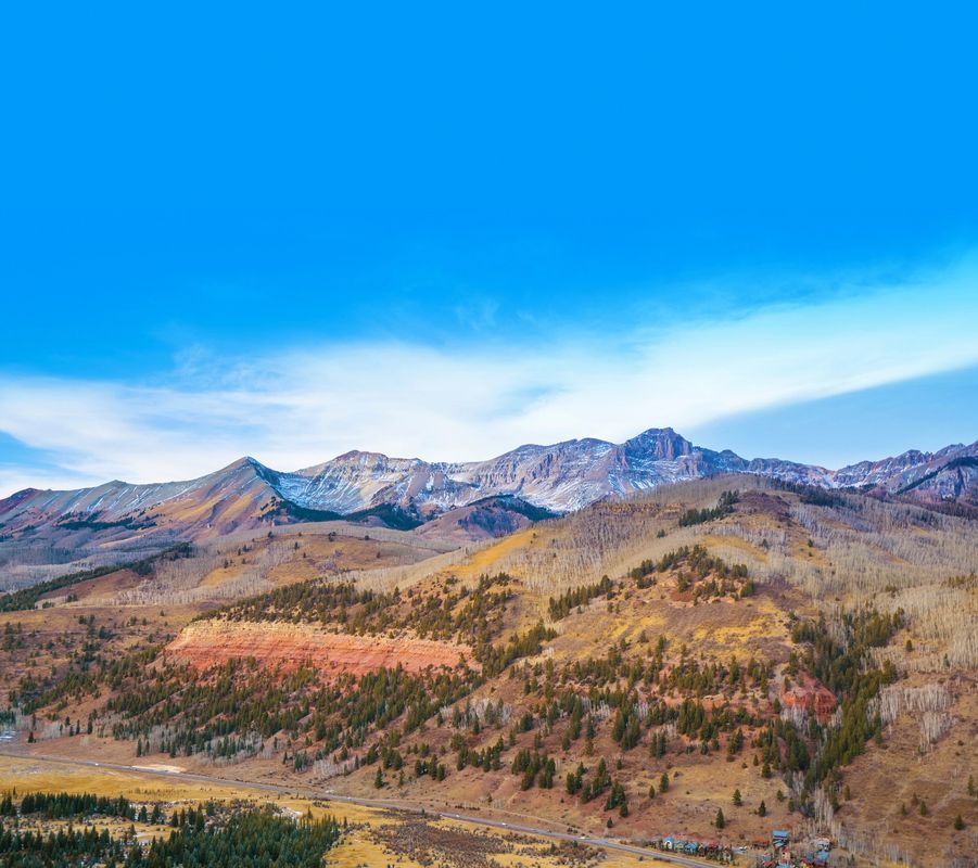 Vibrant mountain range under a clear blue sky with scattered clouds.