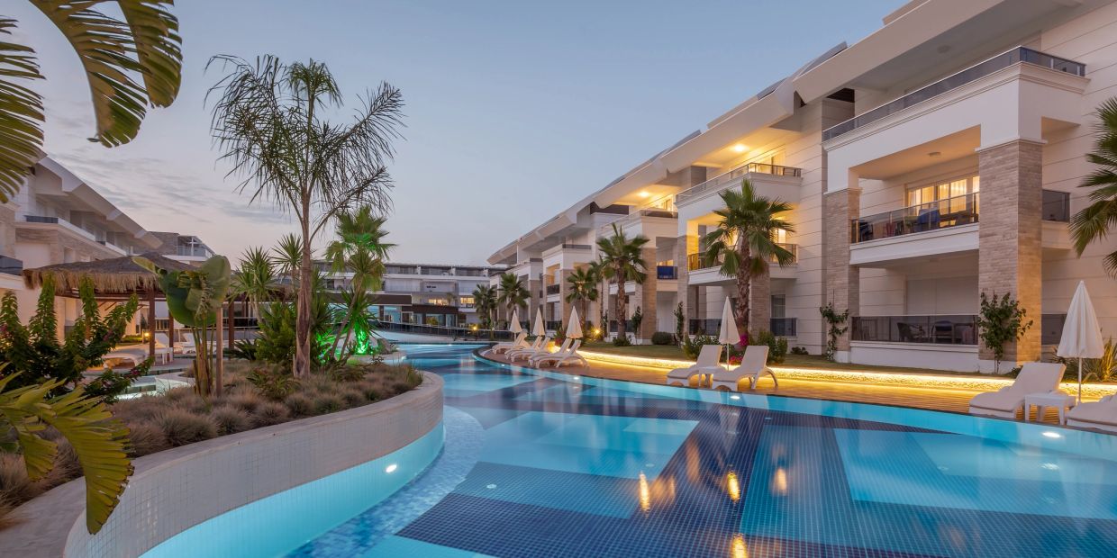Modern resort with illuminated pool and palm trees at dusk.