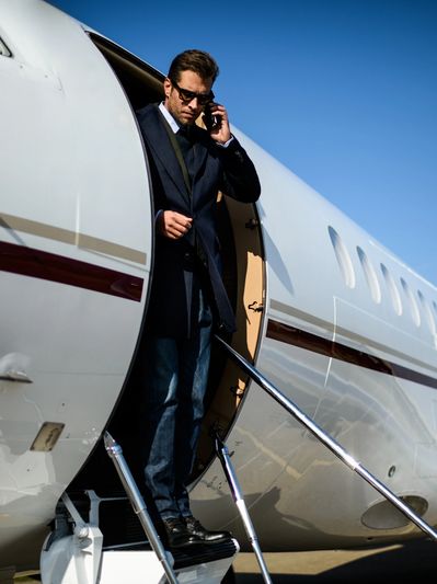 A well-dressed man stepping off a private jet, signaling on-call, high-level travel and concierge se