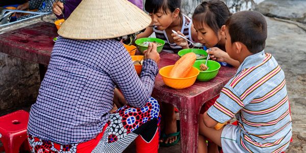 Children and a woman eating together at a low outdoor table.
