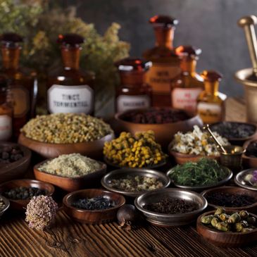 Various dried herbs and spices in bowls with vintage apothecary bottles and a brass mortar and pestle.