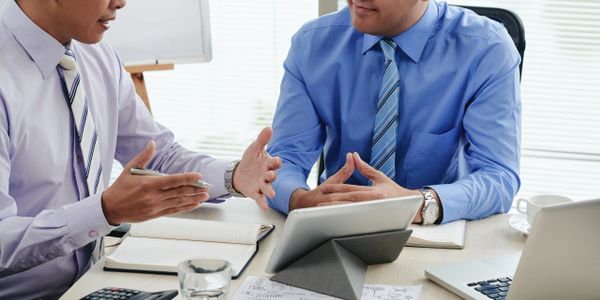 Two businessmen discussing at a desk with documents and devices.
