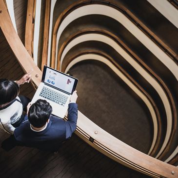 Two professionals reviewing data on a laptop near a spiral staircase.