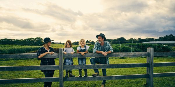 Family enjoying time together on a rural farm fence at sunset.