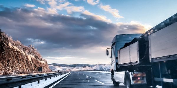 Truck driving on a snowy highway during sunset with a dramatic sky.