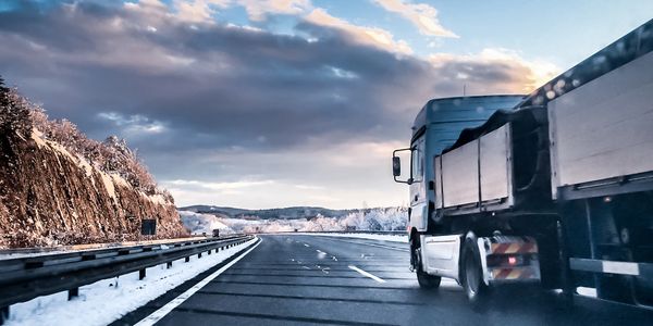 Truck driving on a snowy highway during sunset with a dramatic sky.