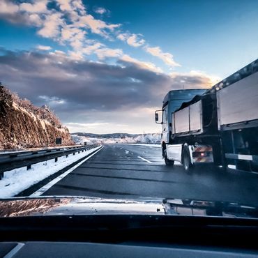 Truck driving on a snowy highway during sunset with a dramatic sky.