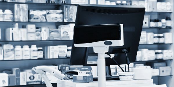 Pharmacy checkout counter with computer screens and product shelves in background.
