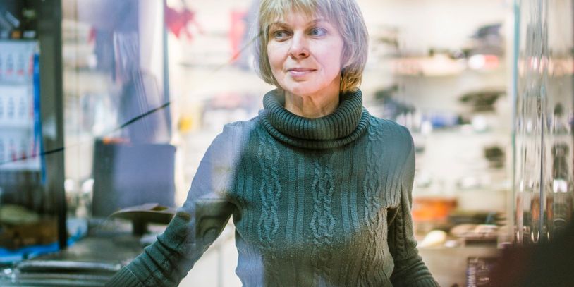A woman in a green sweater stands thoughtfully inside a cozy kitchen.