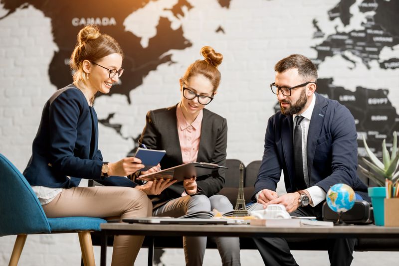 Young businesscouple choosing a trip with agent sitting at the travel agency office with world map on the background