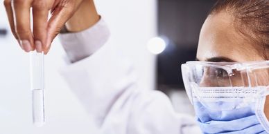Scientist wearing safety goggles and mask holds a test tube with clear liquid.