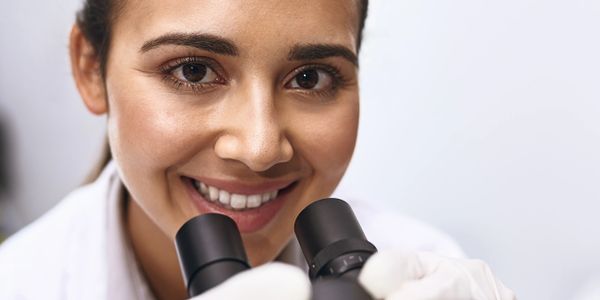 Smiling scientist looking through a microscope in a lab.