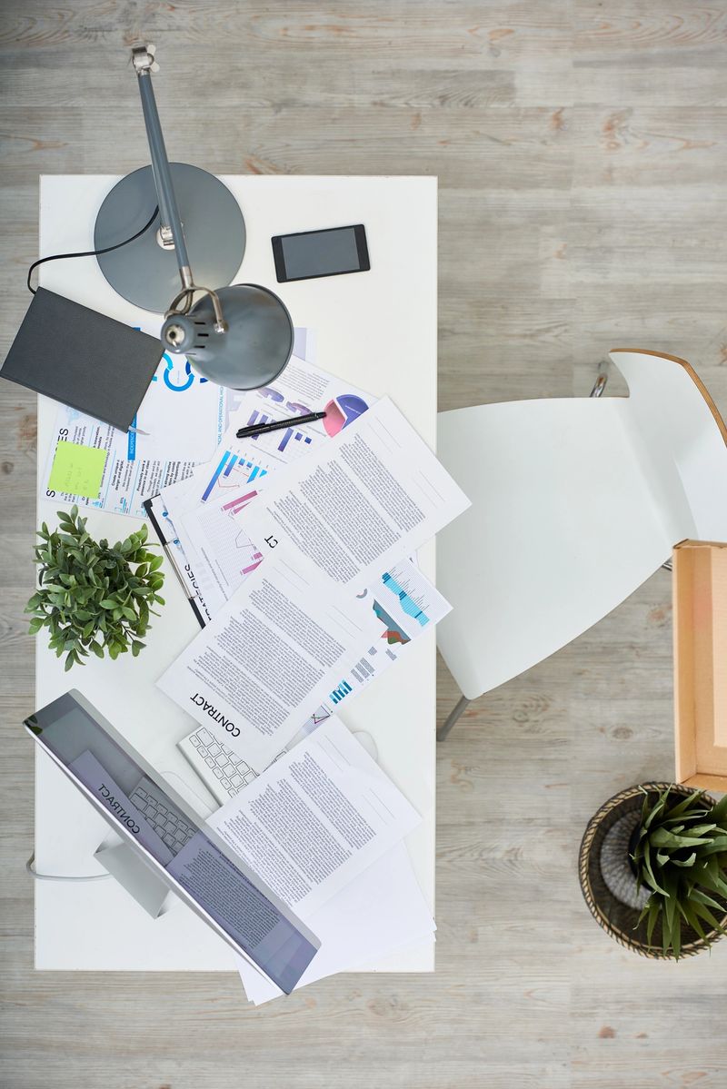 Interior of modern office: wooden desk covered with documents and contracts, chair and houseplant, directly above view