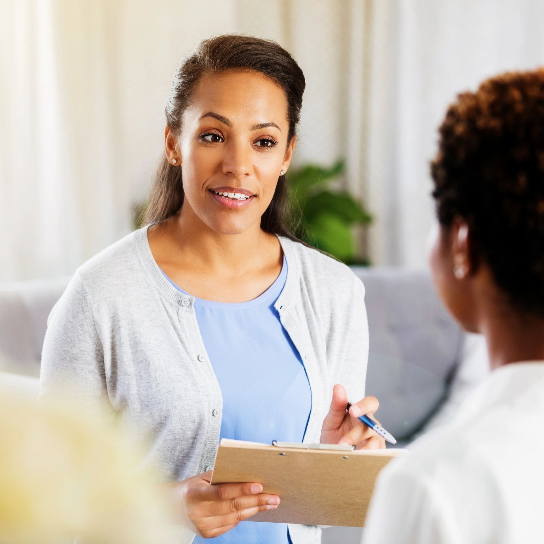 A woman holding a clipboard, engaged in conversation with another person.
