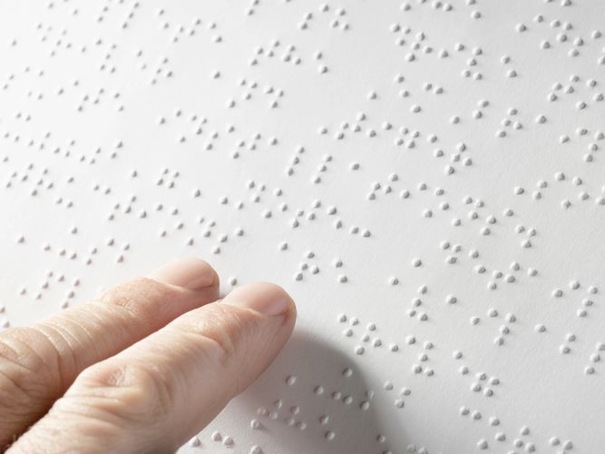 Close-up of fingers reading Braille on white paper.