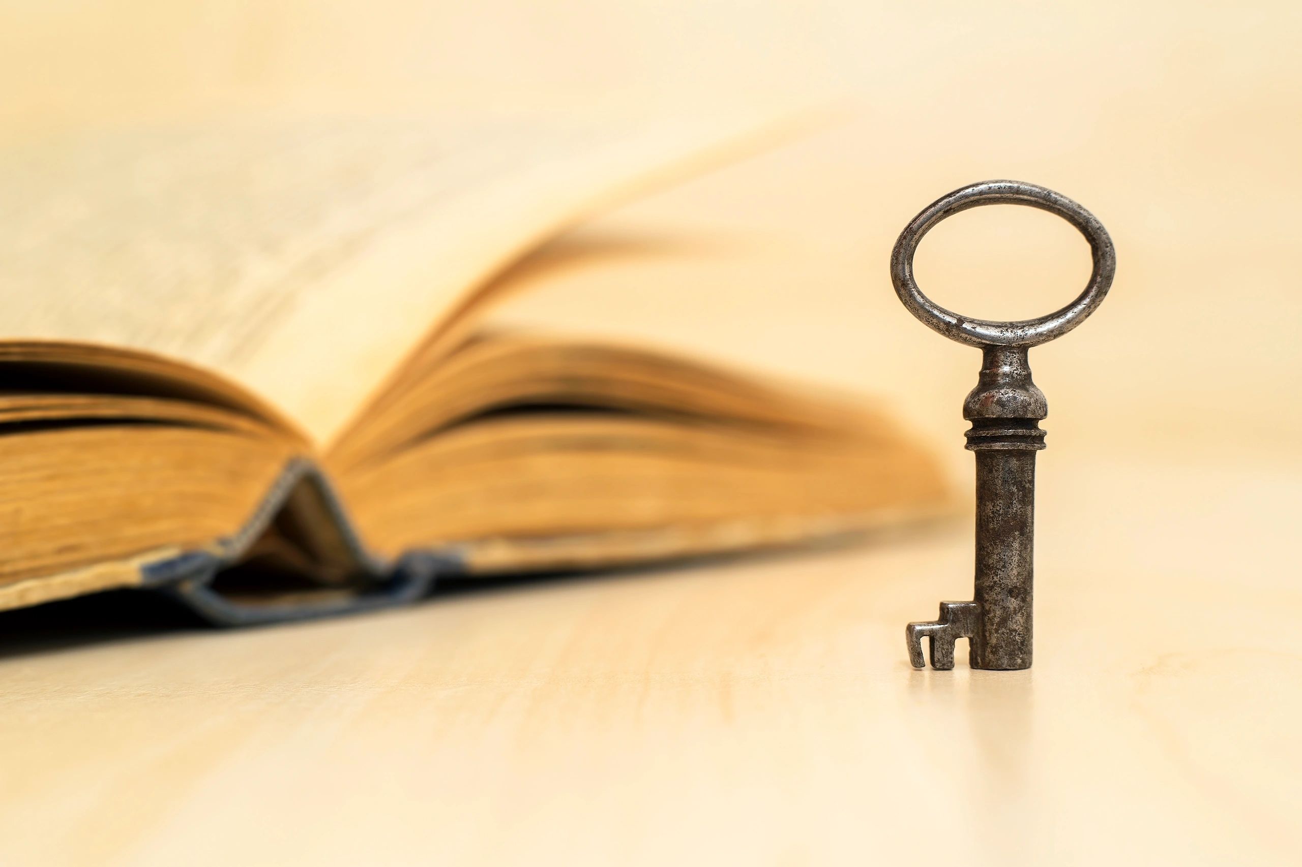 An old key standing in front of an open book with turning pages.