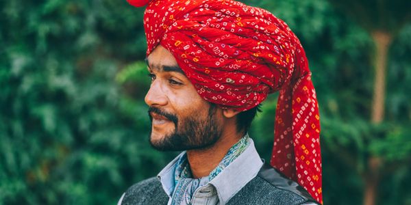 Man wearing a vibrant red traditional turban with a thoughtful expression.
