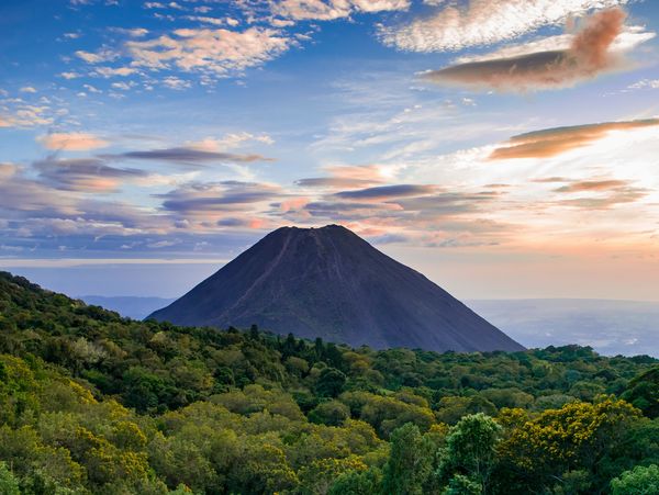 Volcán impresionante al atardecer con bosque verde.