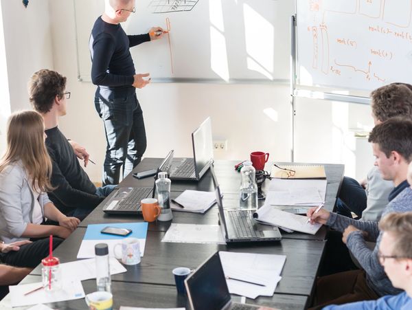A team meeting with a presenter explaining on a whiteboard while others listen.