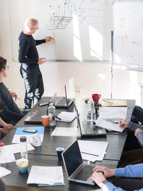 A man explains a concept on a whiteboard to colleagues in a meeting room.