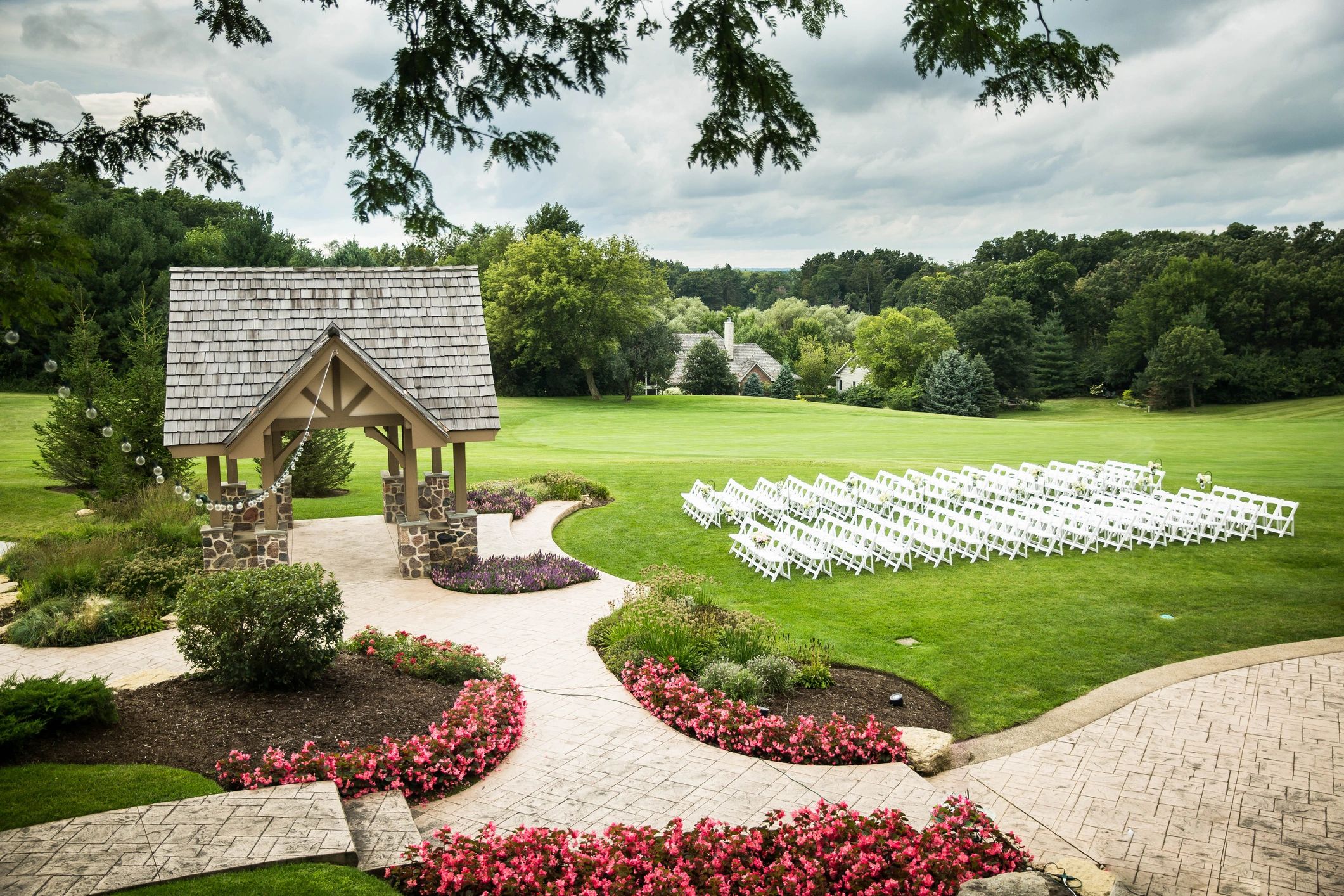 Outdoor wedding setup with white chairs and floral decorations on a green lawn.