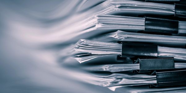 Close-up of stacked documents held by black binder clips.