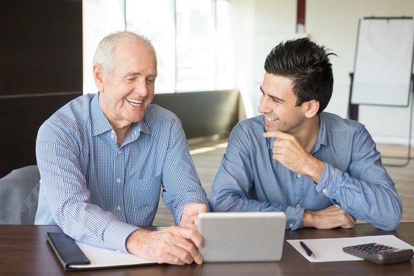 Two men smiling while looking at a tablet.