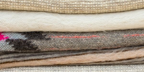 Stack of various textured woolen fabrics in neutral and earthy tones.