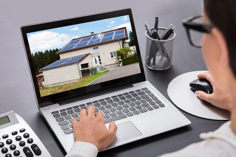 Close-up Of A Businesswoman Looking At House With Solar Panel On Laptop