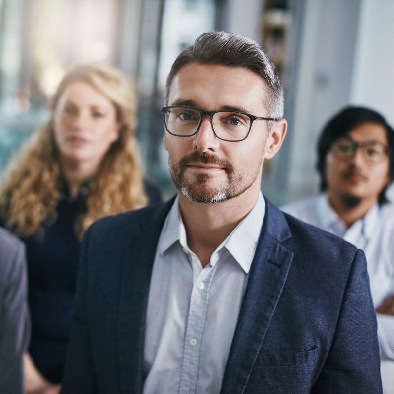 Portrait of a mature businessman standing in an office with his colleagues in the background