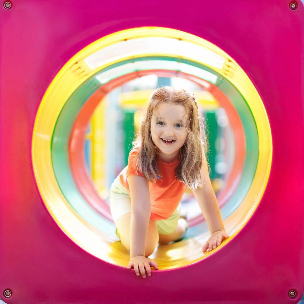 Smiling girl crawling through a colorful playground tunnel.